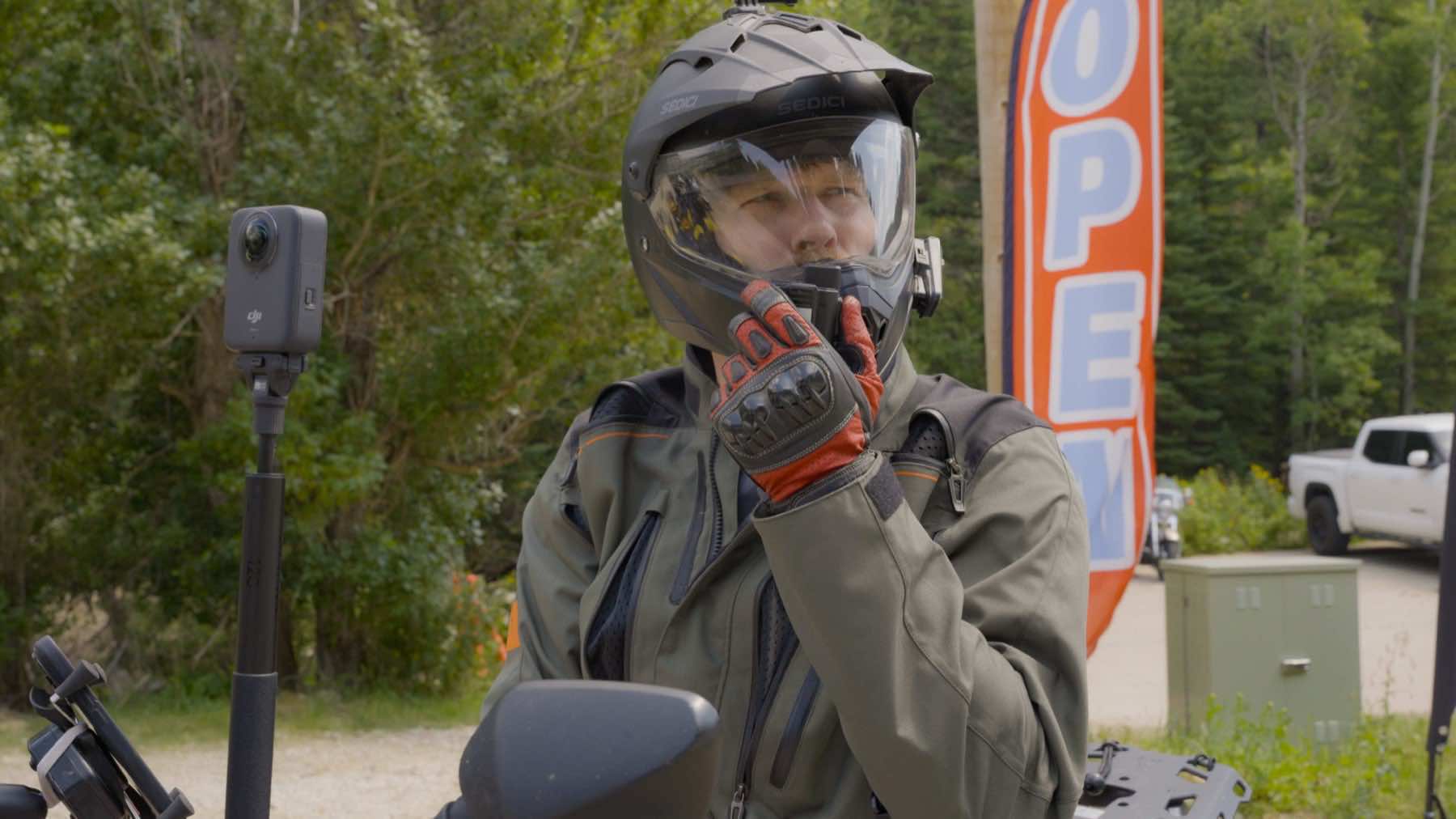 Rider in helmet keying a SkyCom PTT radio mic on an adventure motorcycle