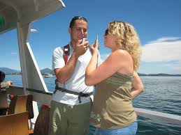 A man and woman engage in a lively conversation on a ferry, with a backdrop of blue water and clear skies, capturing a moment of connection and enjoyment.