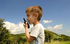Boy using a walkie-talkie outdoors against a clear blue sky, surrounded by lush green hills, suggesting a moment of adventure and communication.