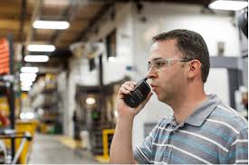 A worker in safety glasses communicates via a walkie-talkie in a busy industrial setting, ensuring operational efficiency and safety.